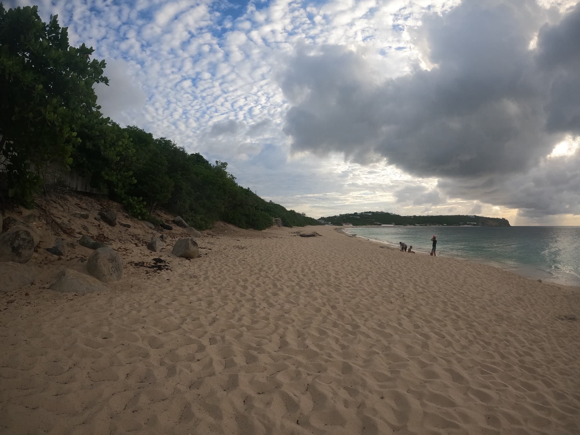 The wide soft-sand beach at Baie Rouge under dramatic clouds