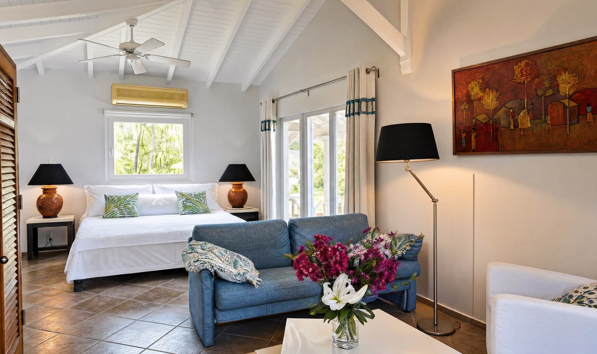 King bed, denim-blue sofa and reading lamps beneath the vaulted white ceiling