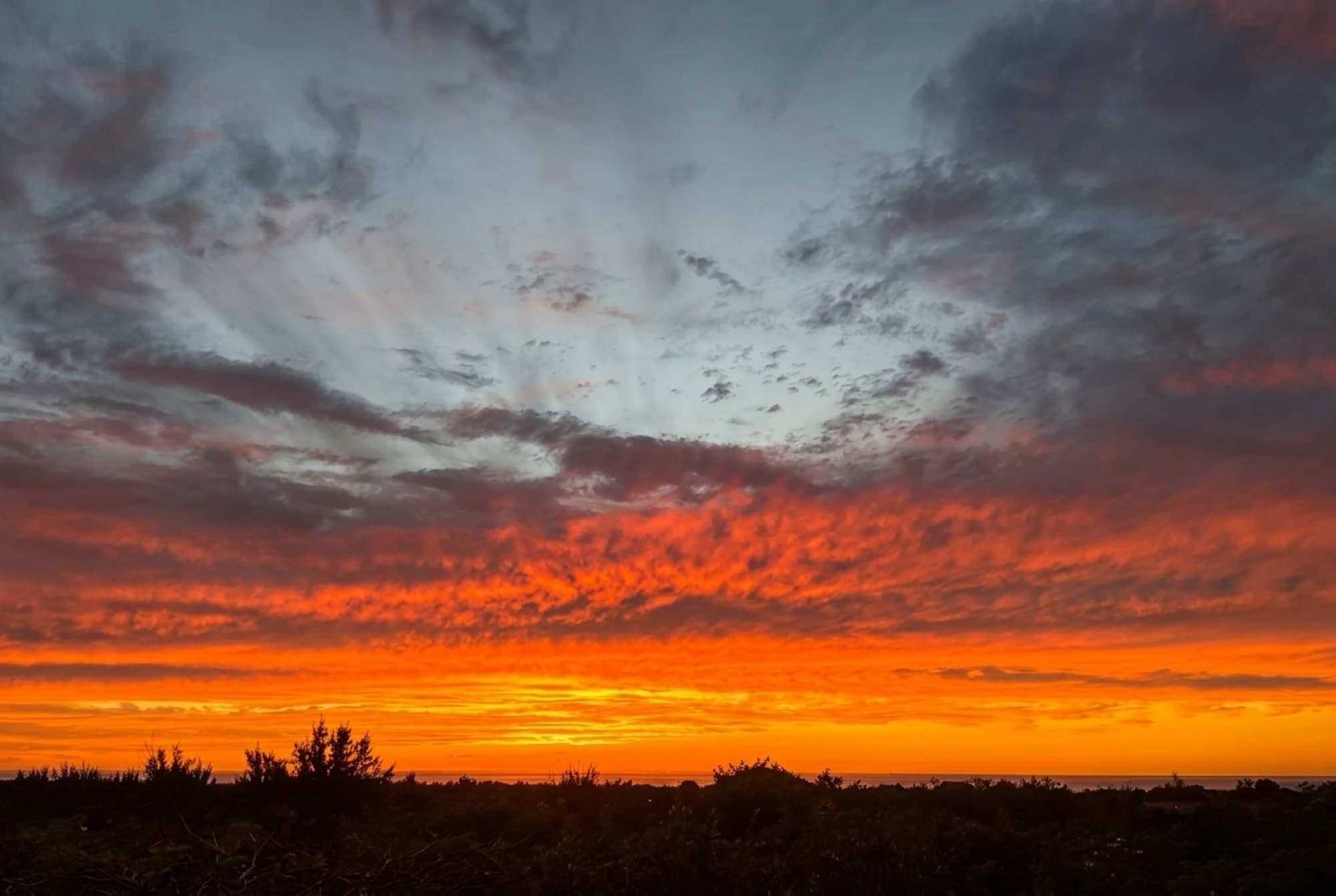 A fiery orange and red sunset sky over the Terres Basses treeline