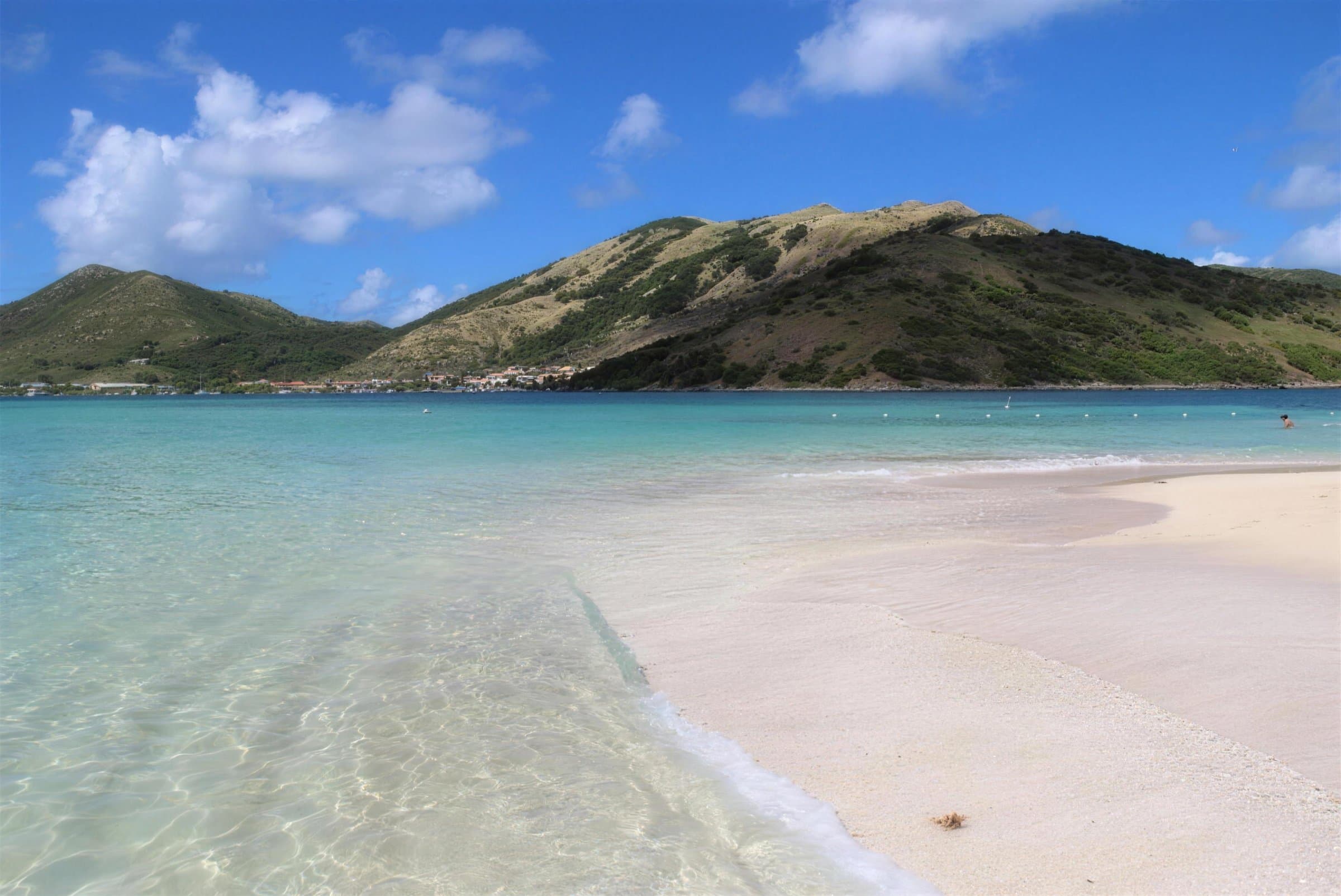 Sable blanc et eau turquoise peu profonde sur l’îlet Pinel, avec les mornes verts de Saint-Martin de l’autre côté du chenal