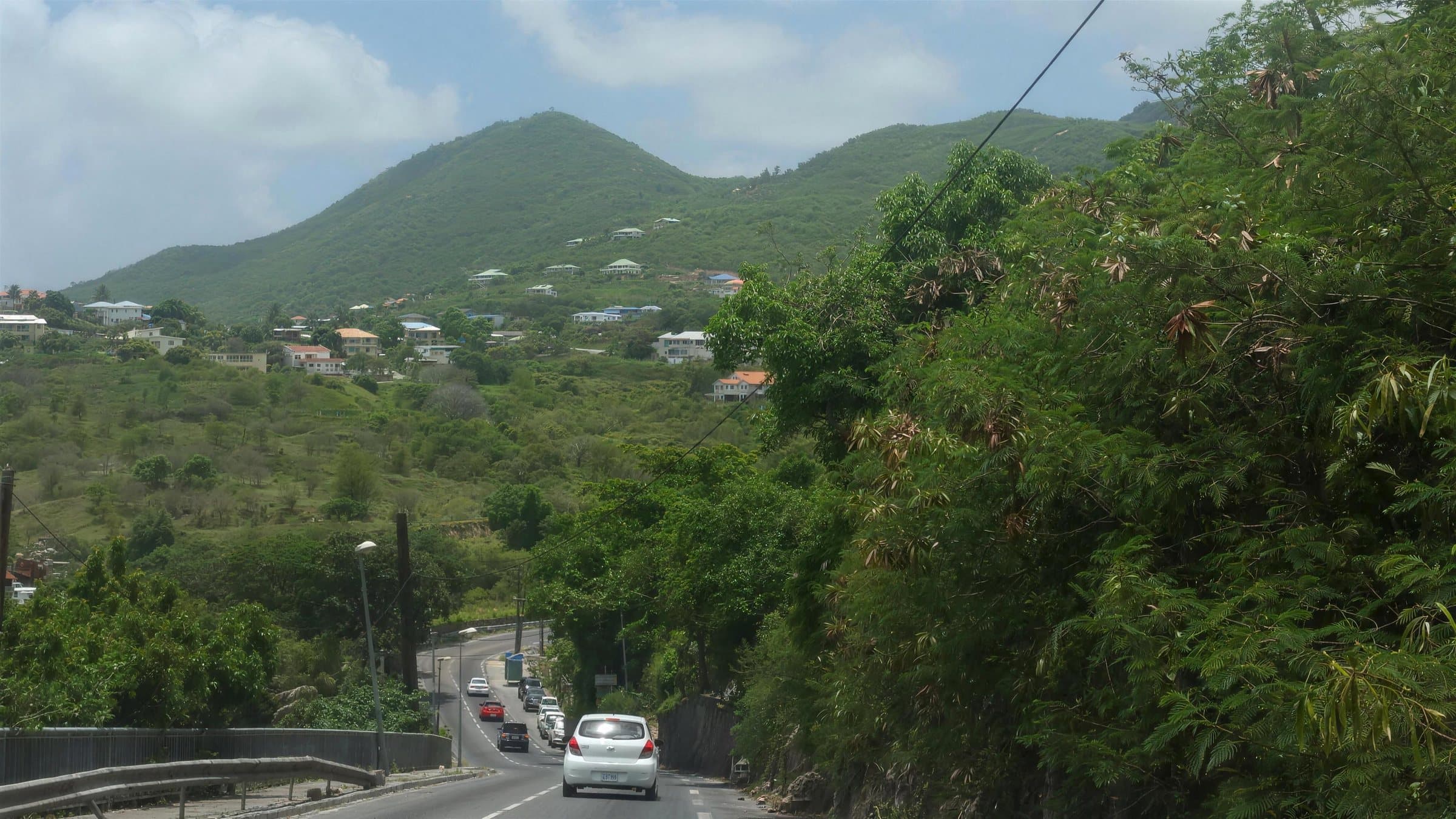A main road winding down through green hills on the French side, with cars in the distance