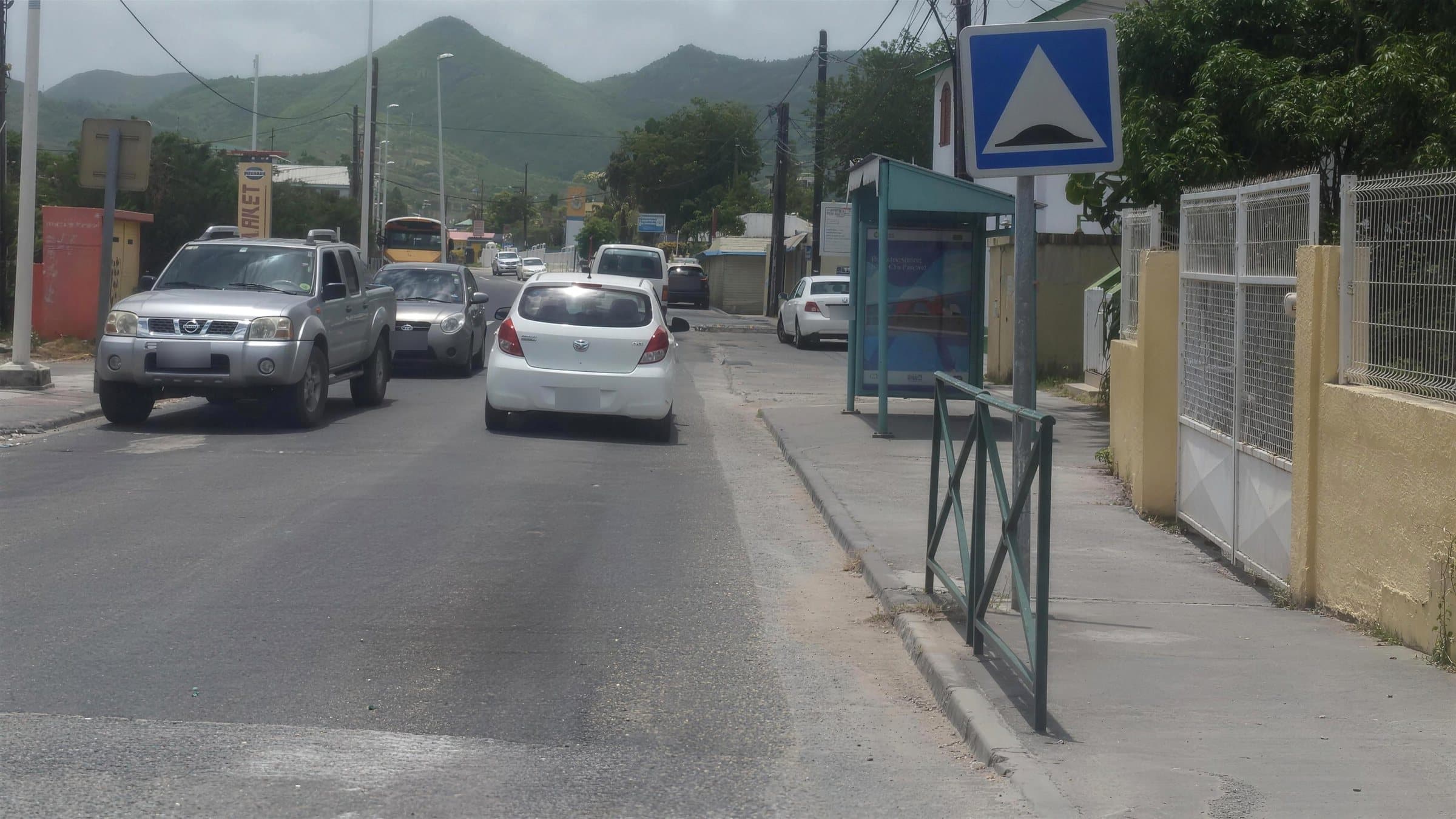 A blue road sign warning of a speed bump beside a town road with traffic