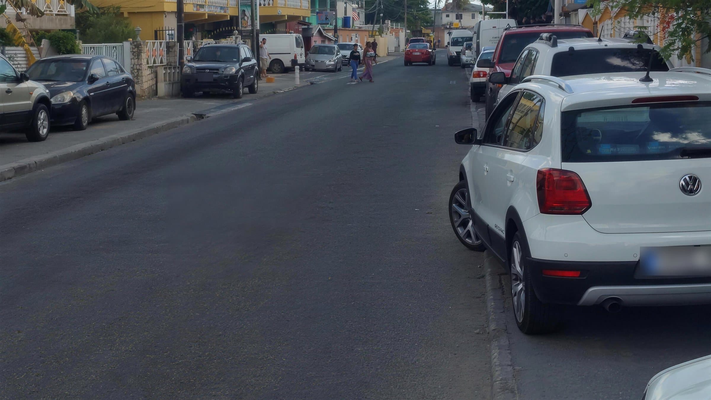 A town street lined with parked cars and shops, with people crossing
